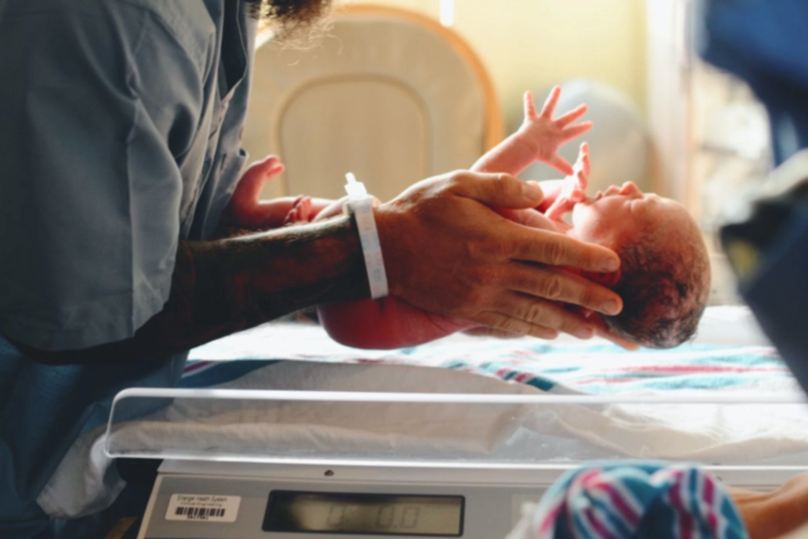 A newborn baby is carefully held by a nurse before being placed on a scale