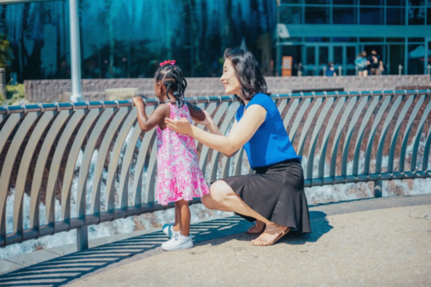 Young girl stands watching a water fountain with her adoptive mother holding her arms