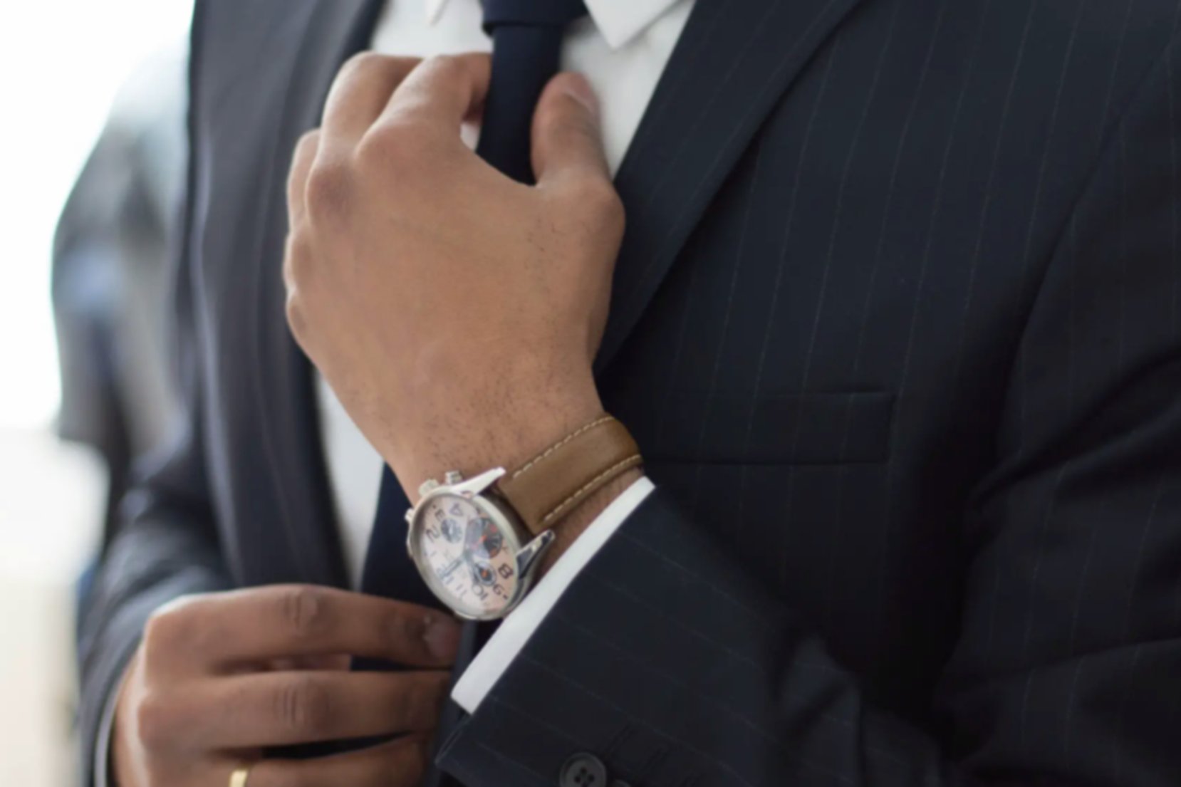 A close-up shot of a man in a smart suit fixing his tie as he gets ready to attend a job interview