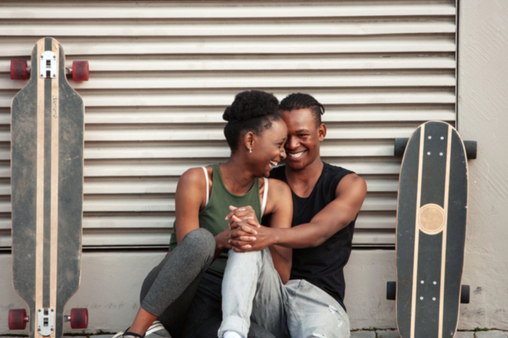 Laughing happy beautiful skater couple sitting on sidewalk in Cape Town, South Africa.