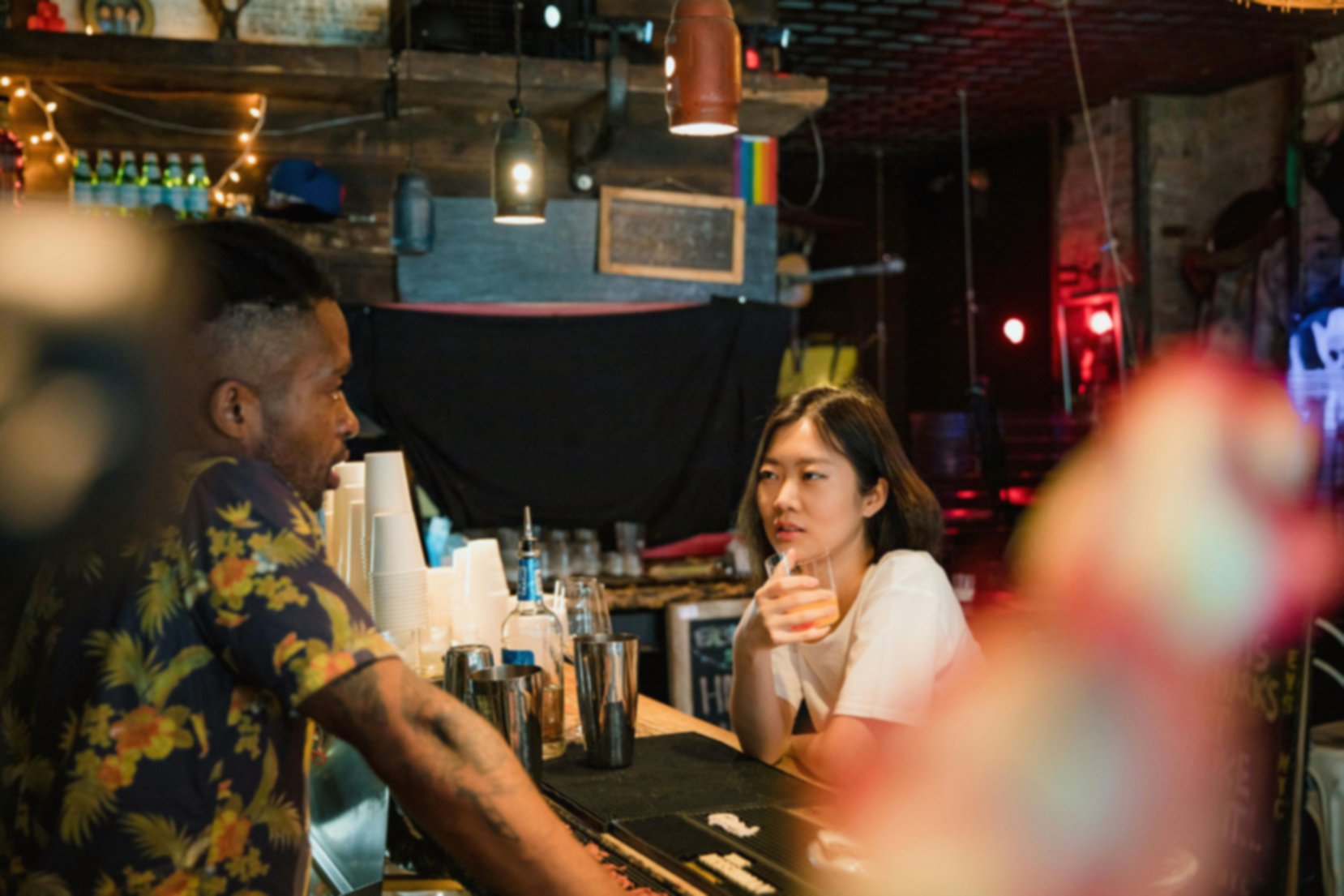Woman sitting at the counter of a bar, talking to the barman.