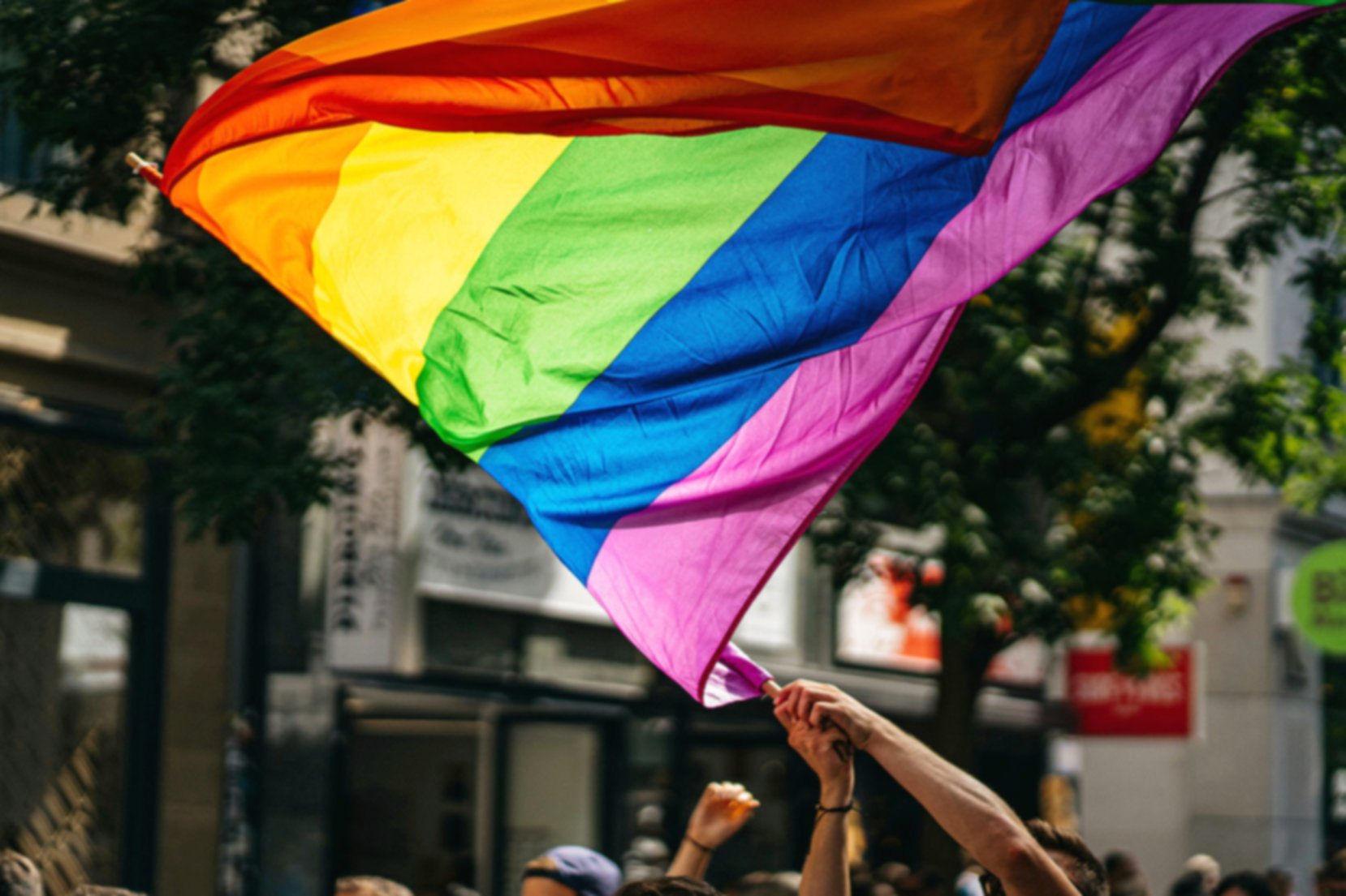 Rainbow flag waving in the wind. It's flying above an invisible crowd.