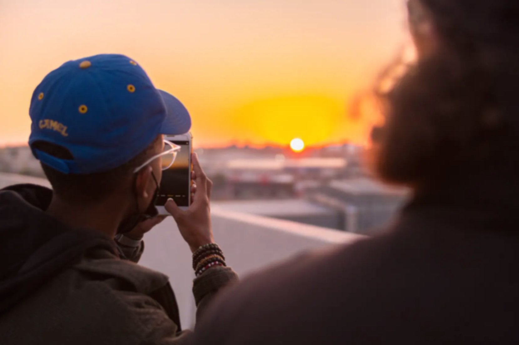 Man using his cell phone to take a picture of the sun set.