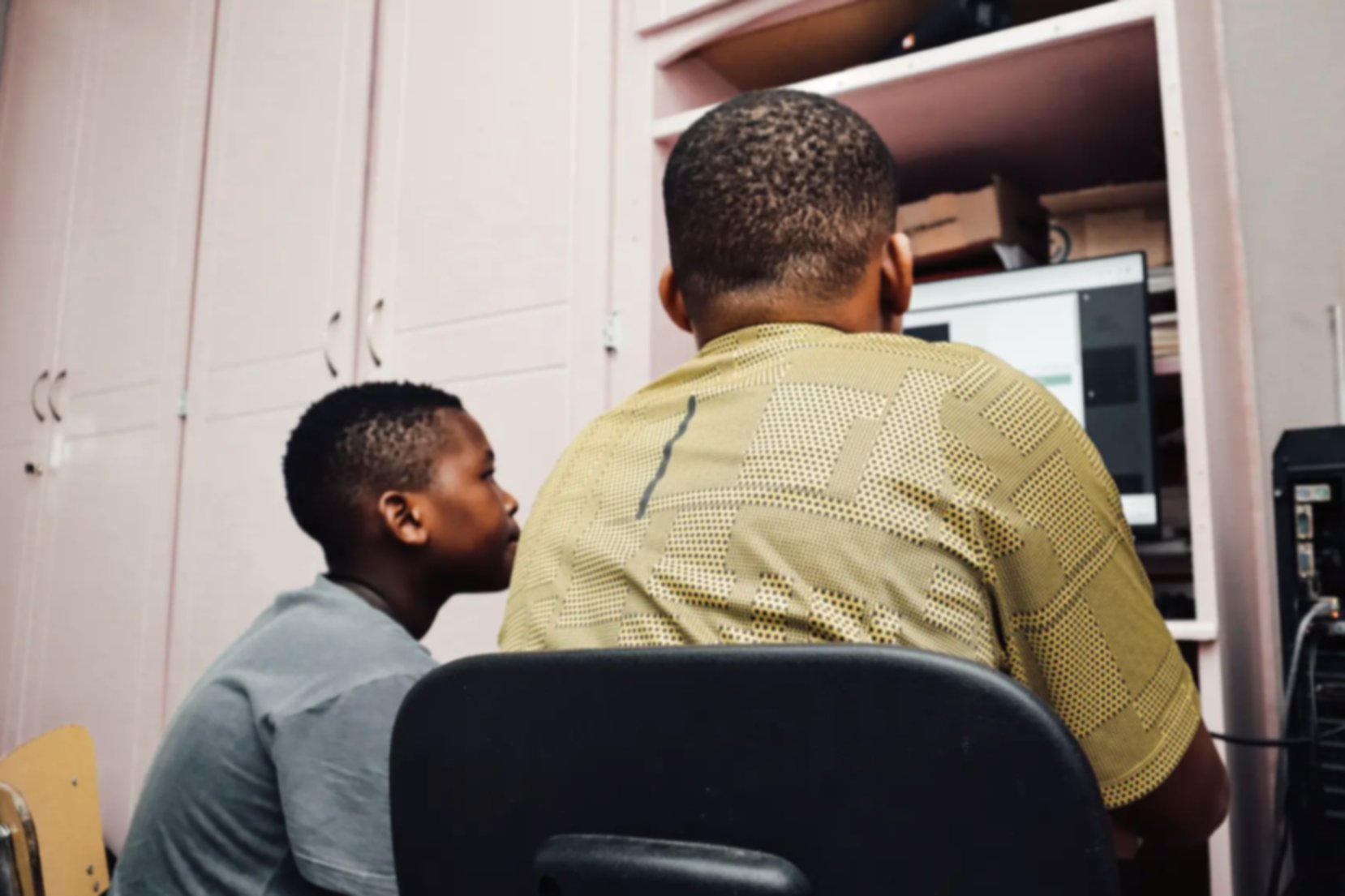 A father and son at home looking at the screen of a desktop computer, using the internet.
