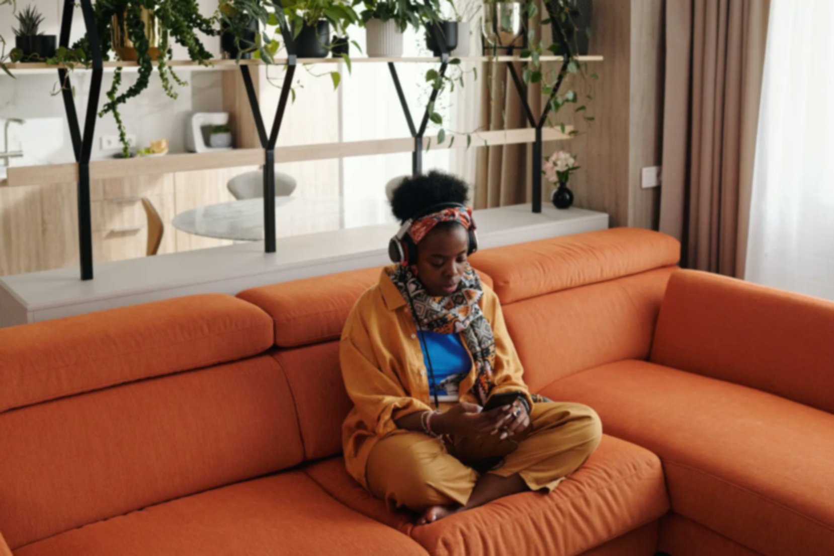 Young women sitting on couch playing with mobile phone while listening to music with headphones